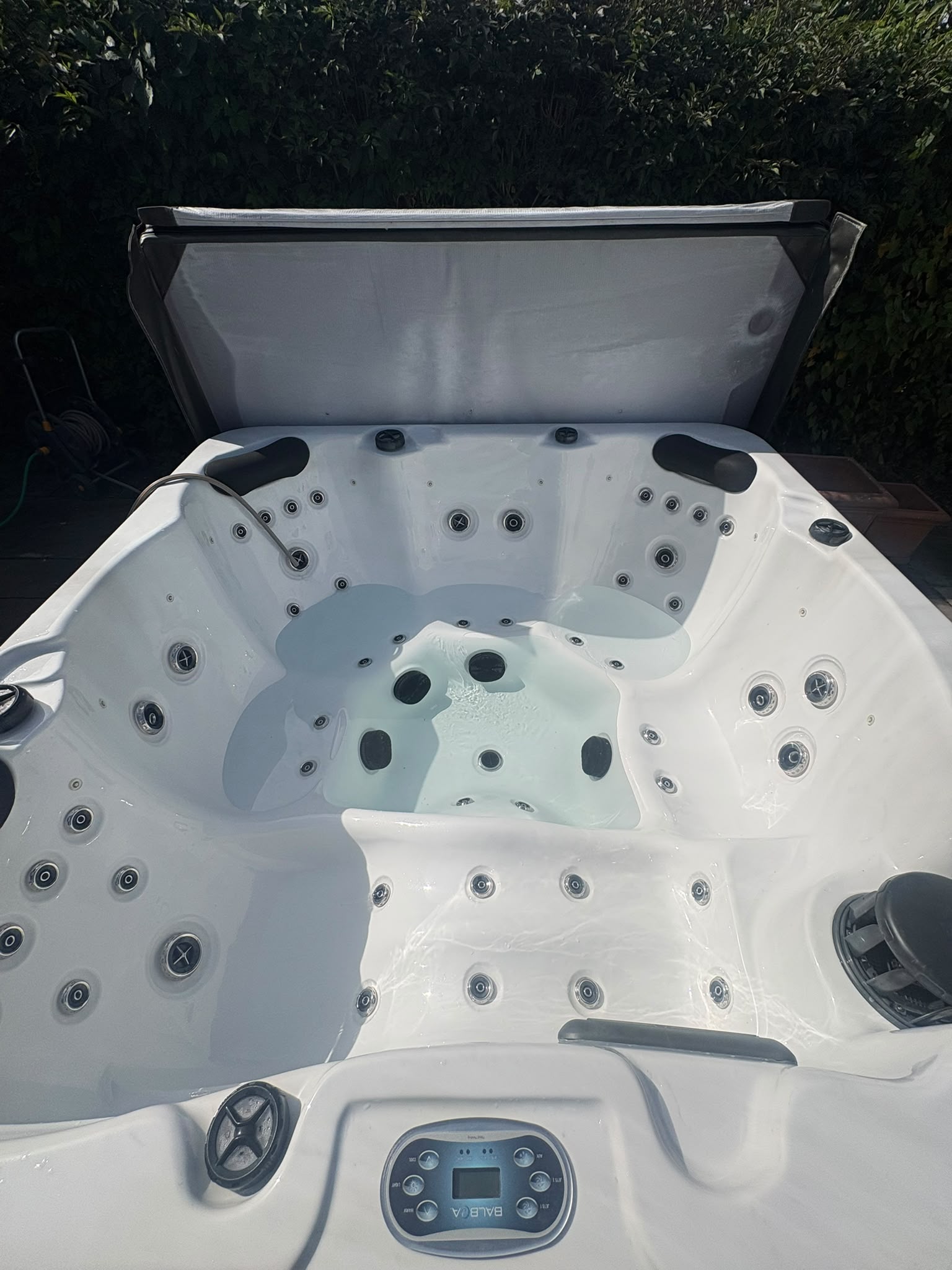 White hot tub shell with seats and jets, an open cover and a hose inside